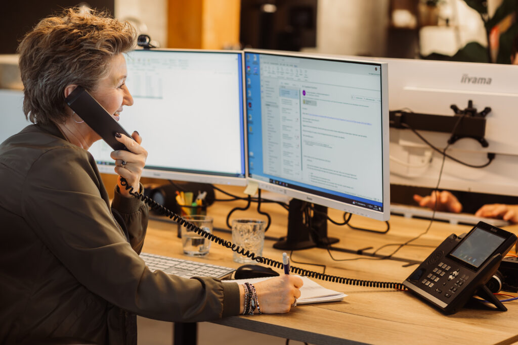 Astrid project manager werkt achter haar pc en belt met klant.